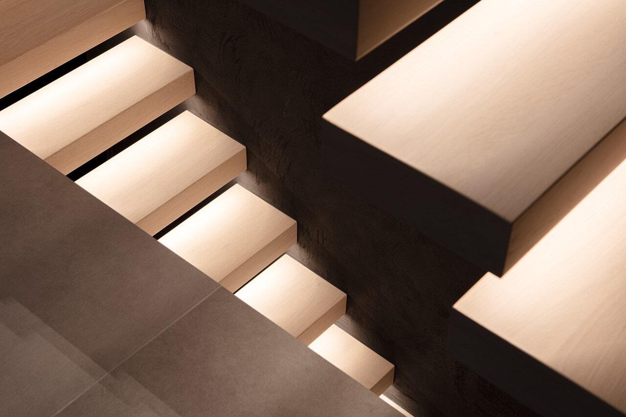 Close-up van moderne zwevende traptreden met warme ledverlichting aan de onderzijde, tegen een donkere muur en grijze vloer.