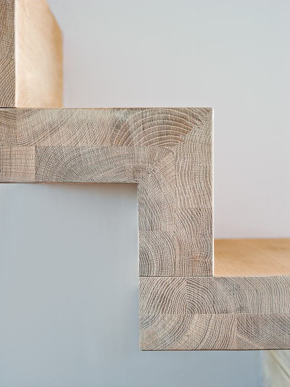 Close-up van de hoekverbinding van een moderne zigzagtrap met licht houten treden en duidelijke houtnerfstructuur tegen een witte achtergrond.